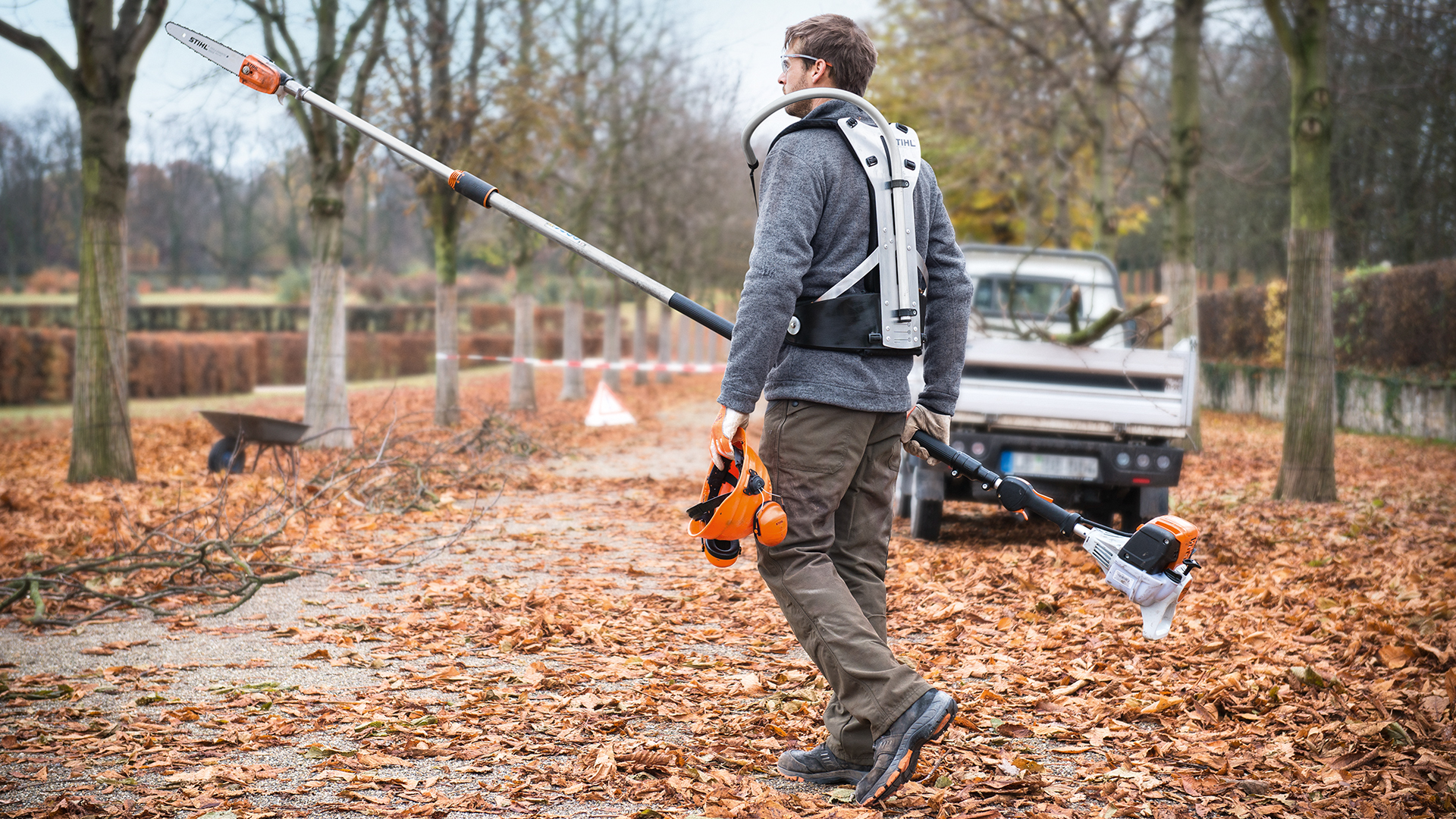 En man med STIHL HT 133 bensinstmkvistare i parken på hösten