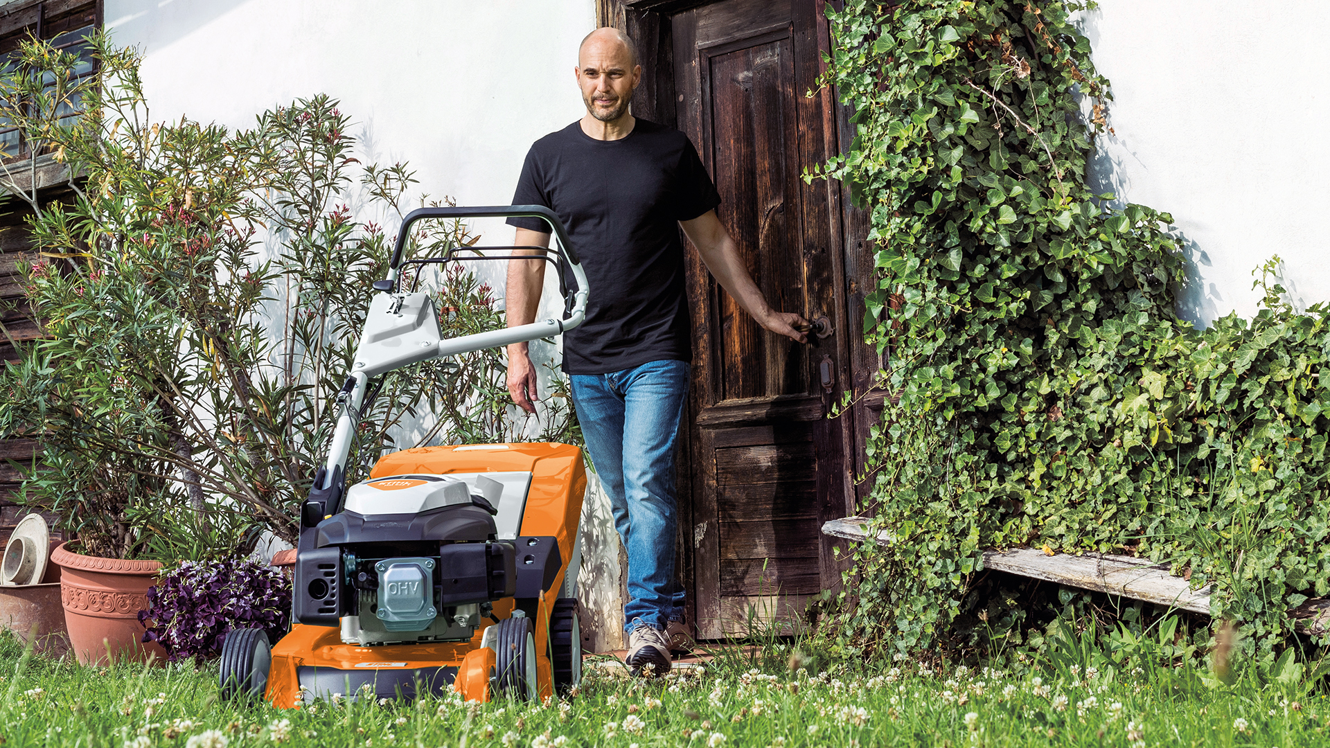 En man går från dörren in i trädgården till en STIHL RM 650 bensingräsklippare