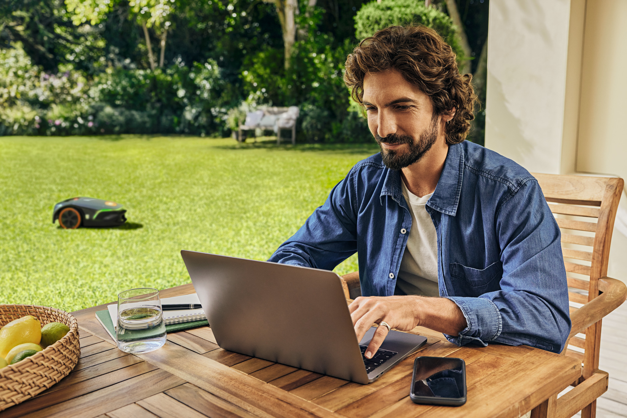 En man arbetar på sin laptop i trädgården.