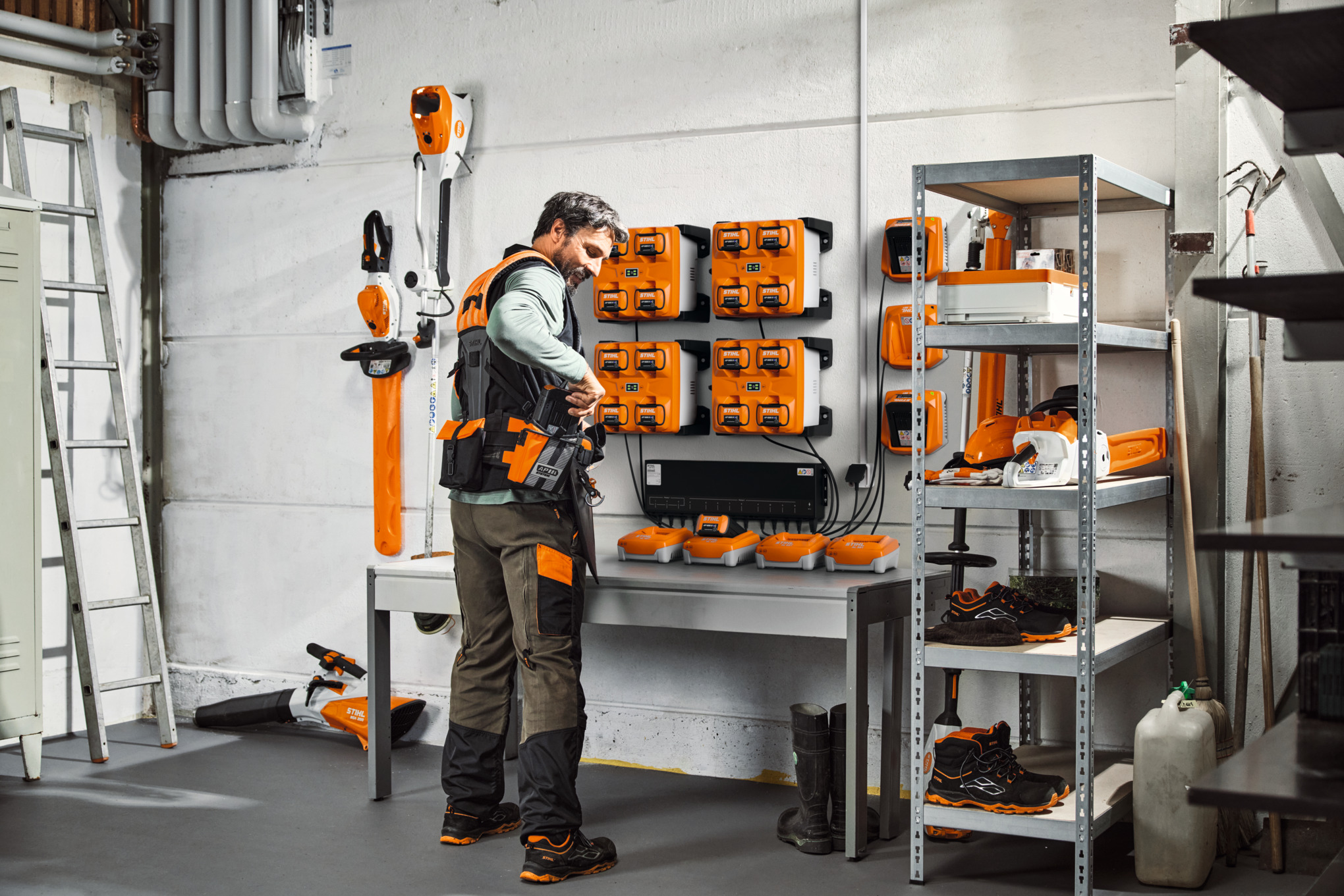 En man i ett förråd med STIHL-verktyg och batterier bär STIHL ADVANCE X-Flex modulära selesystem 