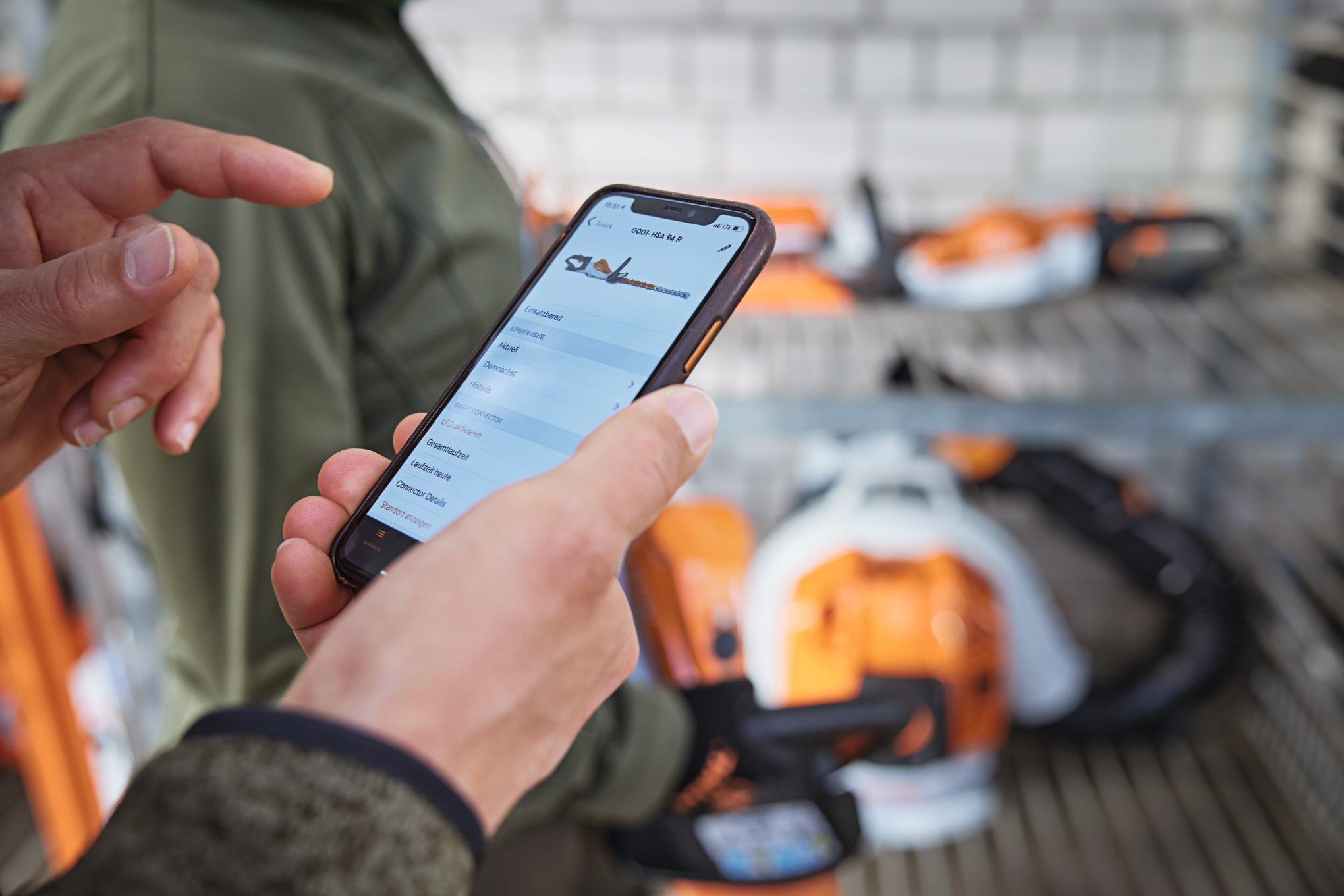 En person med en smartphone som tittar på en motorsåg i STIHL connected-appen