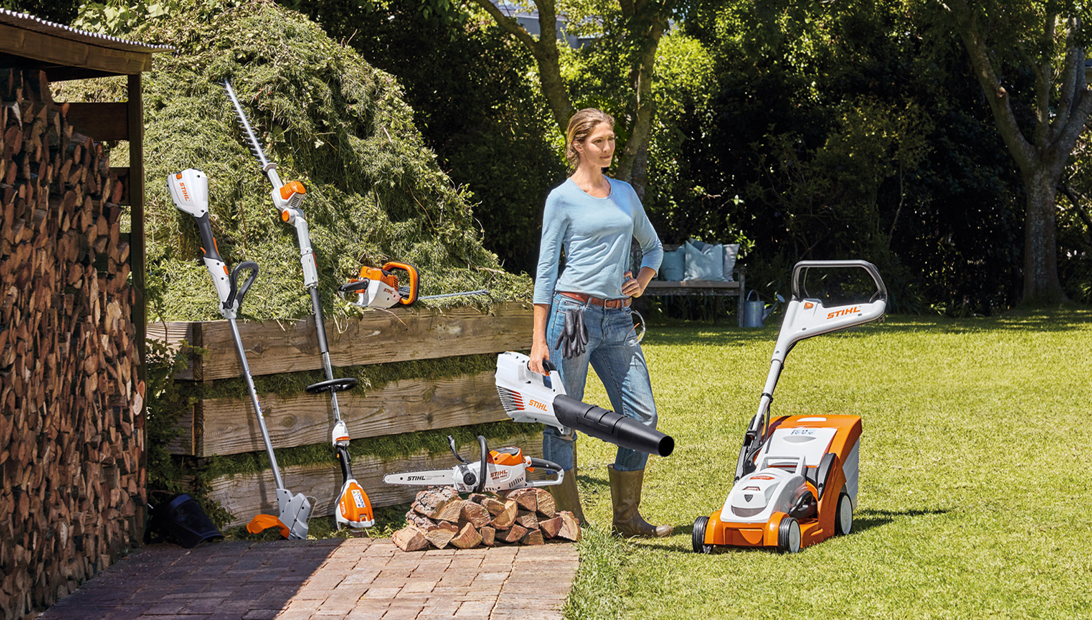 Kvinna som står i trädgården med ett urval av batteriprodukter från STIHL