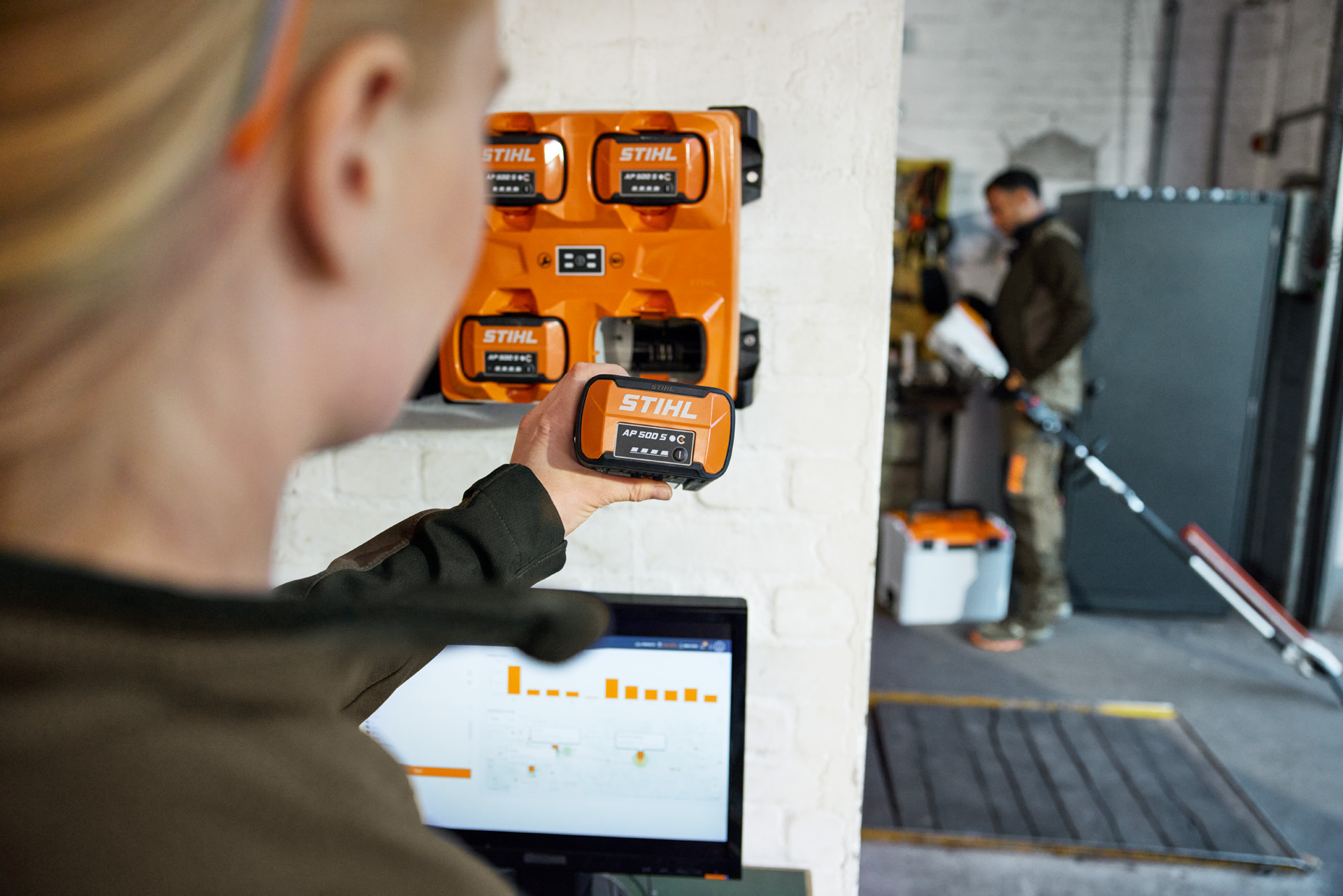 En kvinna framför en bärbar dator som lossar ett AP 300 S-batteri från STIHL AL 301-4 multiladdare