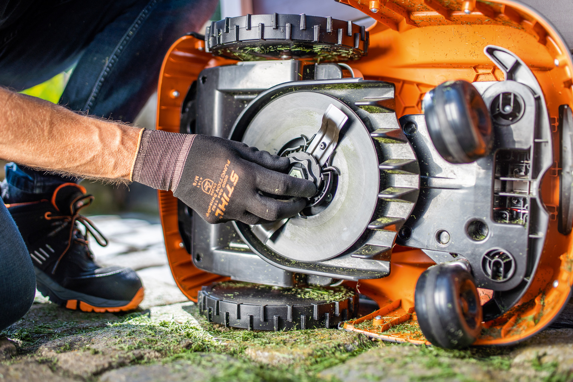 En vy av den rena undersidan av en STIHL iMOW® robotgräsklippare när en person med handskar kontrollerar knivbladet