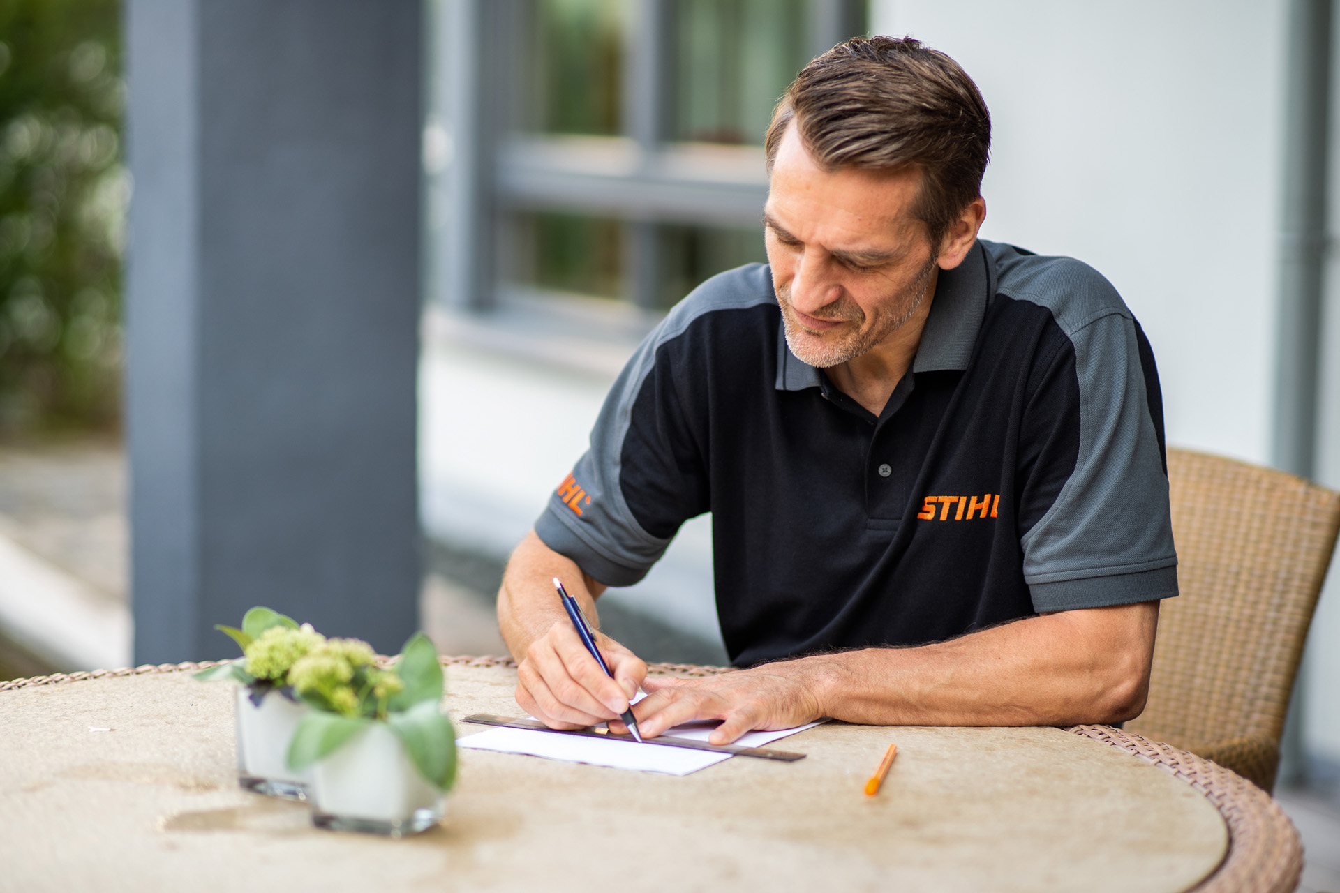 STIHL-återförsäljare sitter vid trädgårdsbord och skapar en plan för gräsmattan som ska klippas av en iMOW robotgräsklippare