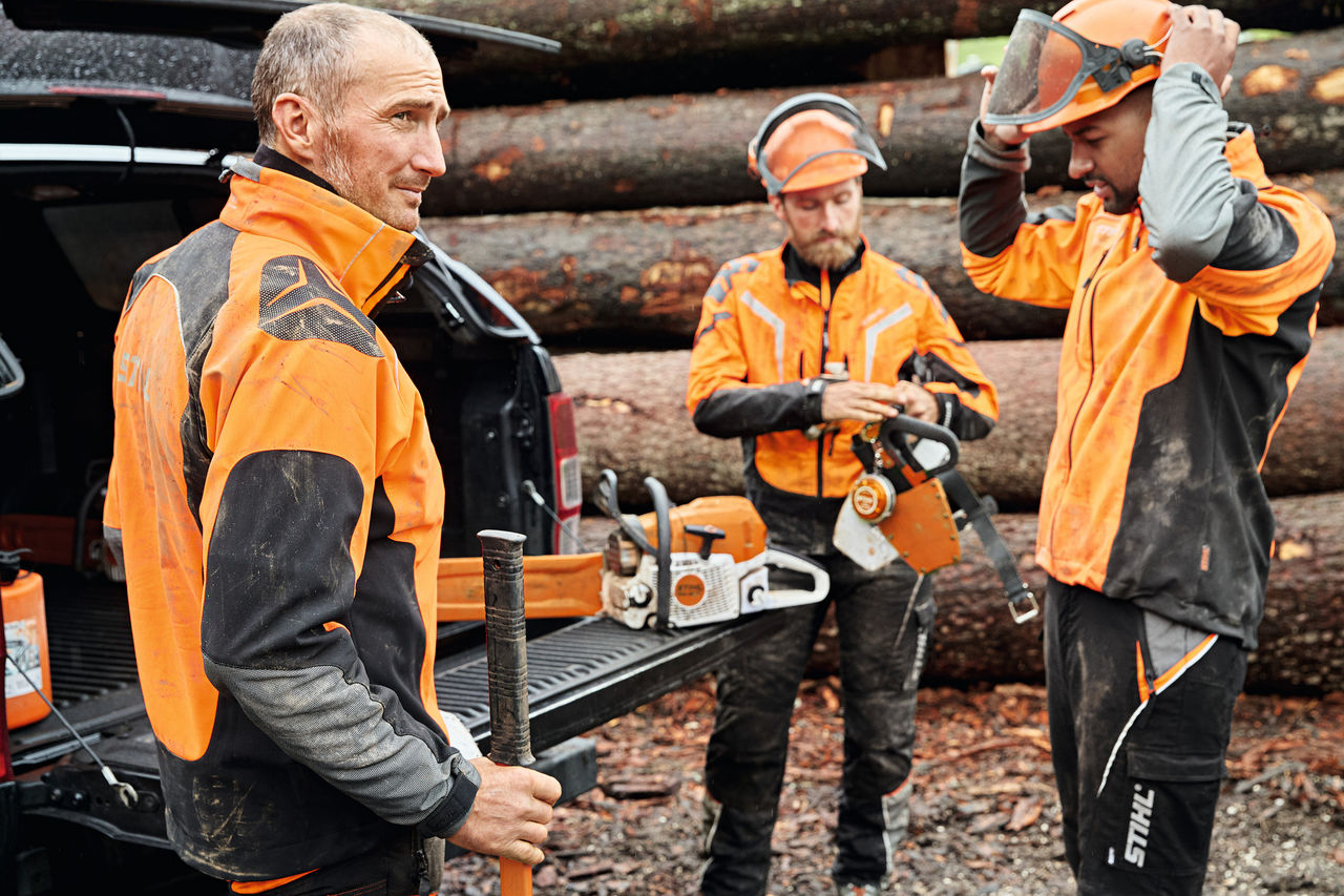 Tre män med skyddsutrustning framför ett fordon med öppet bagageutrymme med STIHL batteridrivna maskiner