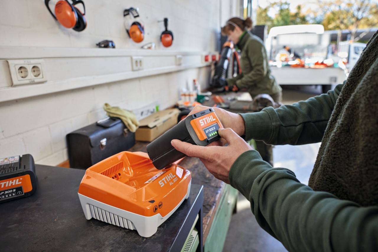 En person ansluter ett STIHL AP 300 S-batteri till en STIHL AL 301 snabbladdare