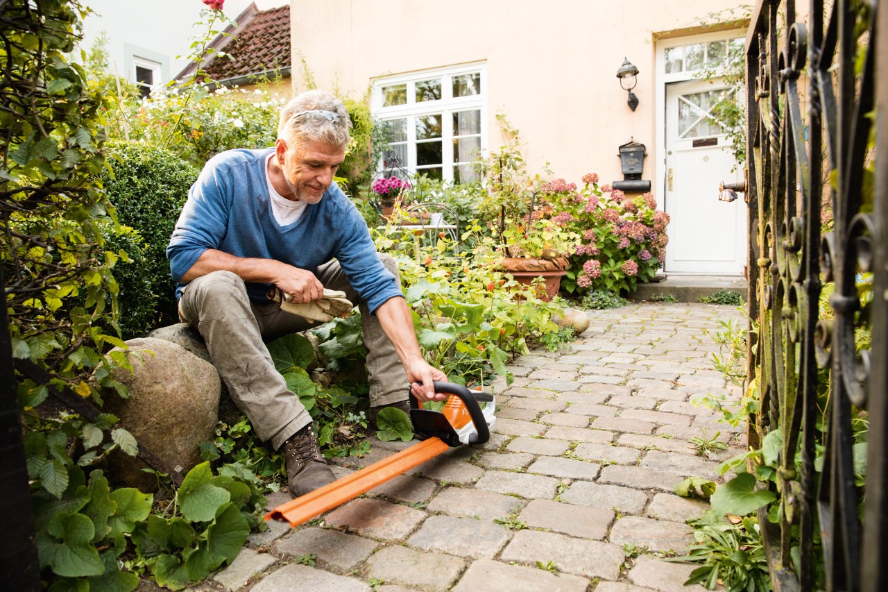 En man som sitter på en stor sten framför ett hus med den batteridrivna häcksaxen HSA 45 i STIHL AI-serien