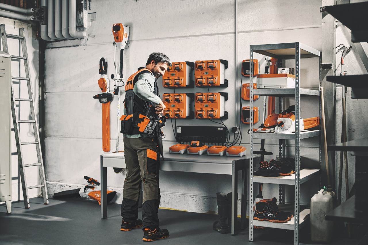 En man som bär det modulära selsystemet STIHL ADVANCE X-Flex i ett förvaringsrum med maskiner och batterier från STIHL 