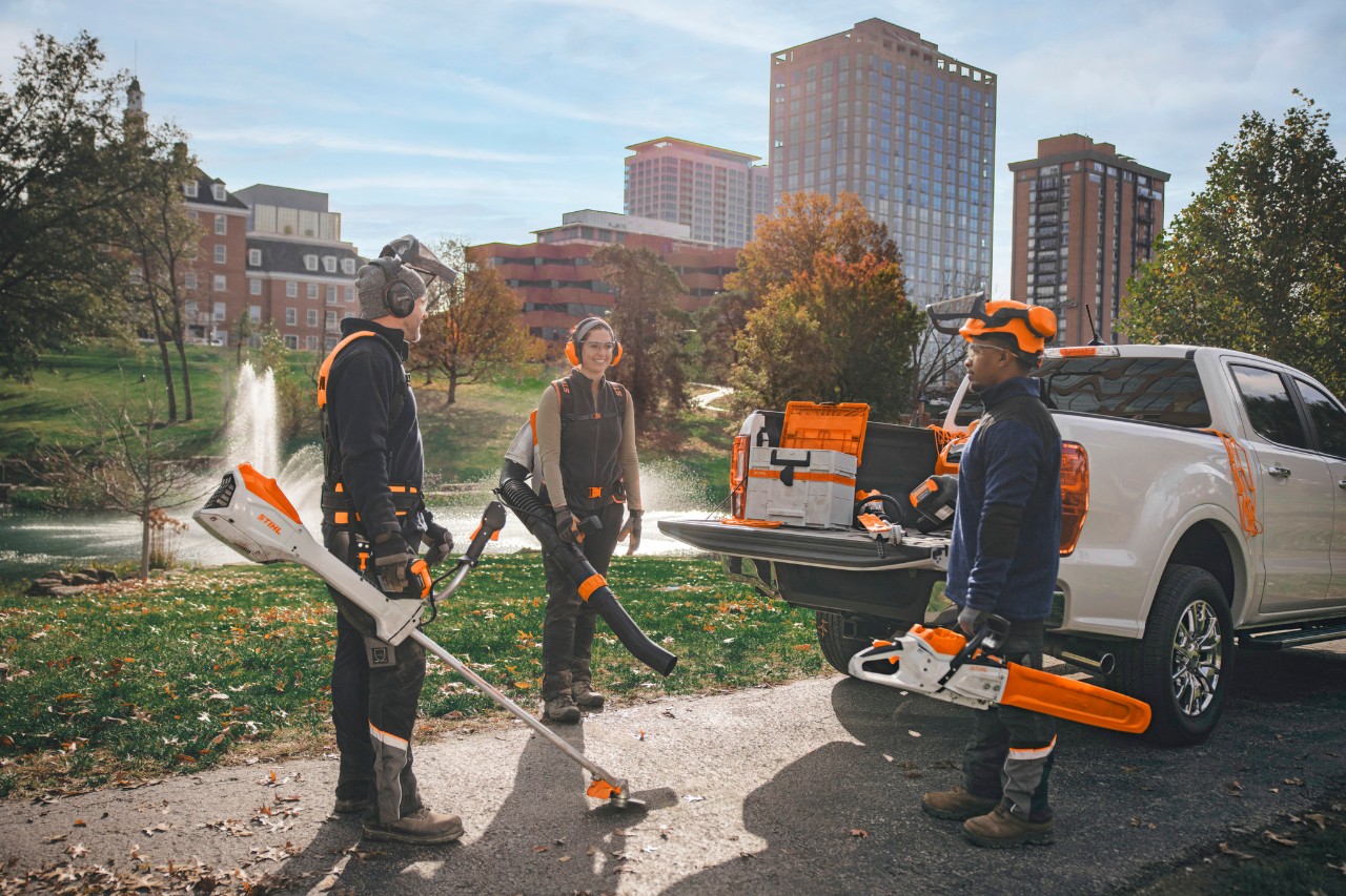 En grupp professionella landskapsarkitekter står runt sina fordon och gör sig redo för arbete med STIHL sladdlösa verktyg.