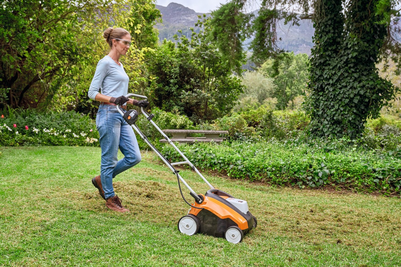Kvinna med skyddsglasögon och arbetshandskar klipper en äng med en STIHL gräsklippare