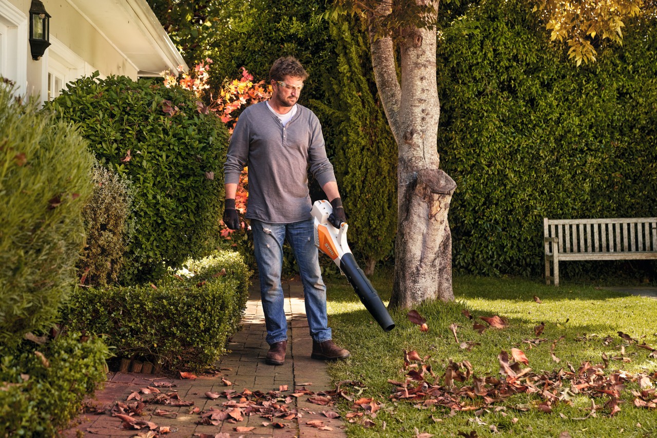 Ein Mann bläst mit einem Akku-Blasgerät STIHL BGA 57 Laub von einer Rasenfläche